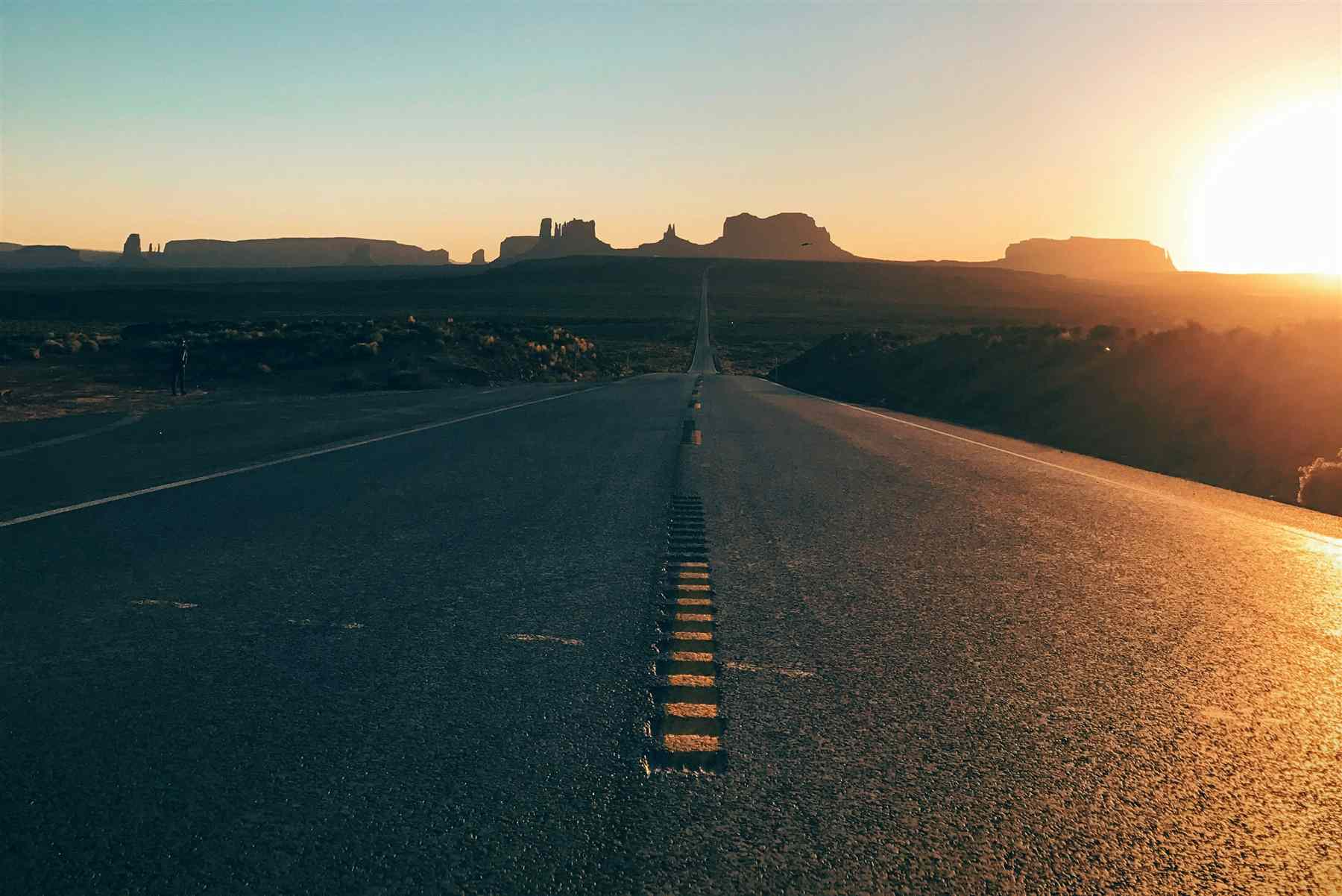 Open desert highway leading toward Monument Valley at golden hour