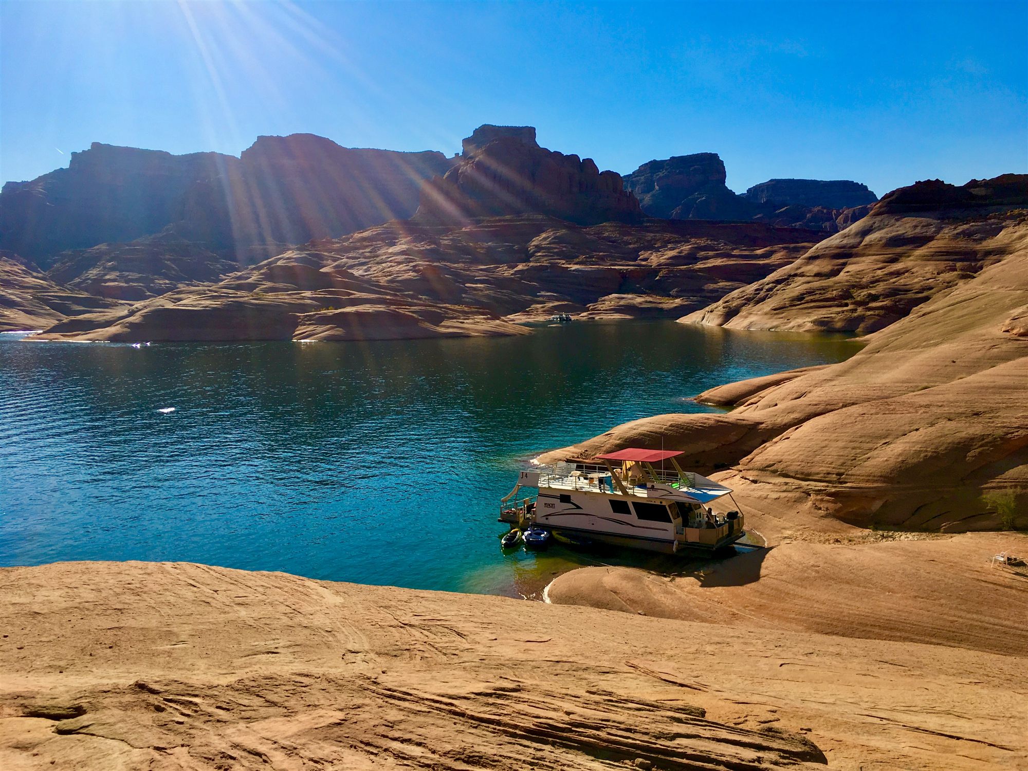 A houseboat moored in a turquoise cove of Lake Powell, surrounded by sandstone cliffs, Arizona